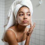 Young woman enjoying a refreshing skincare routine with face cream in a modern bathroom.